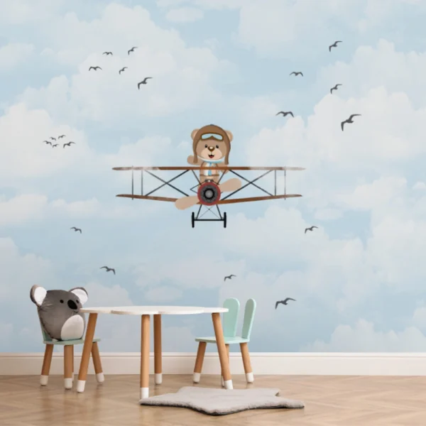 Papel de parede infantil com ursinho aviador voando em um céu azul com nuvens e pássaros