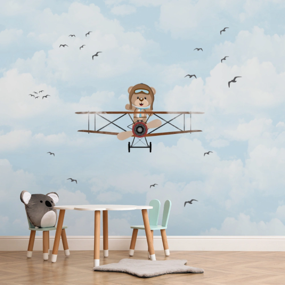 Papel de parede infantil com ursinho aviador voando em um céu azul com nuvens e pássaros